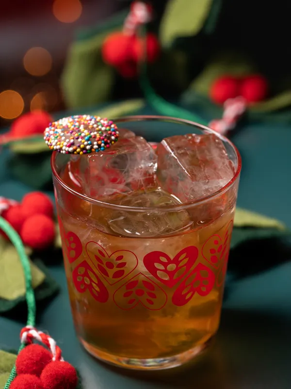 At the Christmas Bar in Toronto, Project Gigglewater 
              serves a festive cocktail with ice in a charming glass, 
              adorned with a chocolate disc covered in colorful sprinkles and 
              surrounded by decorative elements.