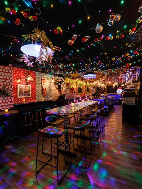 Step into a Toronto Christmas bar wonderland at 
            Project Gigglewater, where the festively decorated interior sparkles with 
            colorful lights, hanging ornaments, cozy stools at the counter, and walls 
            adorned with framed pictures.